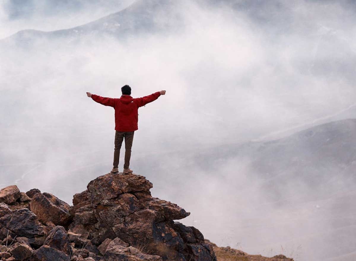 person with arms up standing on a rock looking up at mountain
